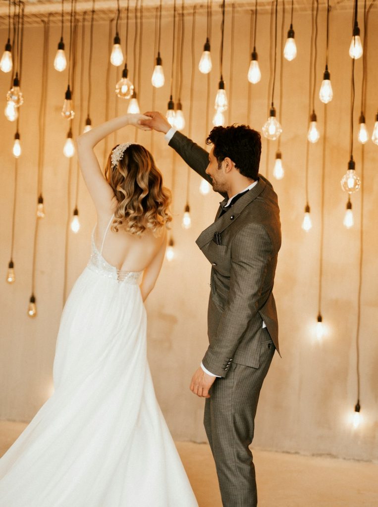 a-bride-and-groom-dancing-in-front-of-hanging-lights-nltxcf2alr0