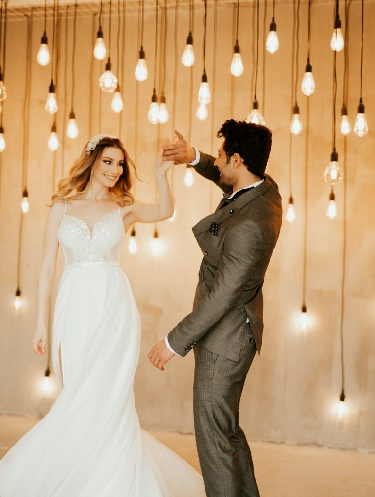 a-bride-and-groom-dancing-in-front-of-hanging-lights-zu-crarbdxa